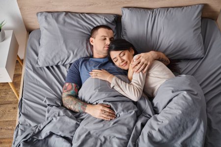 Draufsicht auf junge und glückliche gemischtrassige Paare, die zu Hause auf dem Bett schlafen, Familienglück-Konzept