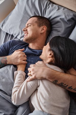 top view of young overjoyed interracial couple embracing in bedroom at home, family happiness