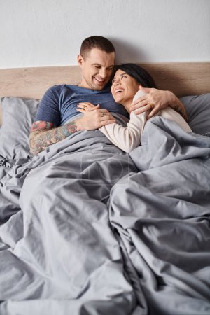 junges multiethnisches Paar, das sich im heimischen Schlafzimmer umarmt und lacht, Vertrauen und Verständnis