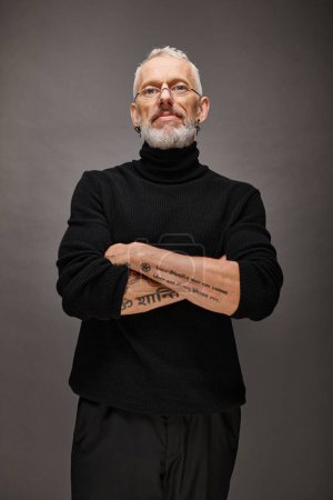 elegant stylish mature man with gray beard and glasses in trendy turtleneck looking at camera