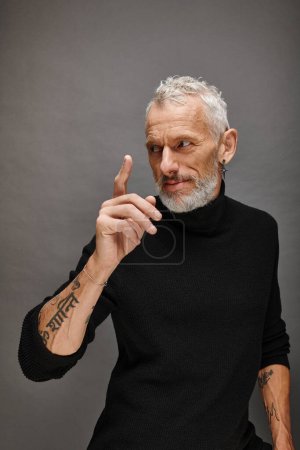 gut gekleideter attraktiver älterer Mann in modischem Rollkragen posiert und schaut vor grauem Hintergrund weg