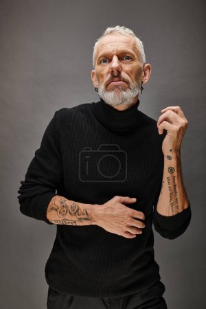 attractive fashionable mature man with beard in chic black turtleneck posing and looking at camera