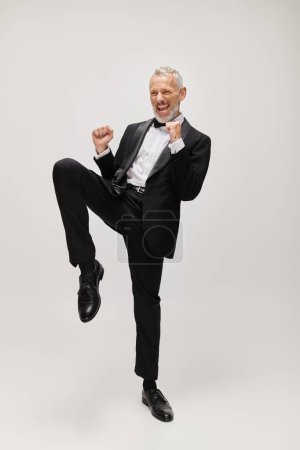 handsome joyful mature man with elegant dapper style with beard dancing happily on gray backdrop