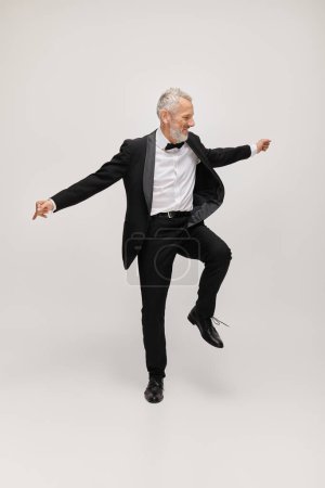 attractive jolly mature man with elegant dapper style with beard dancing happily on gray backdrop