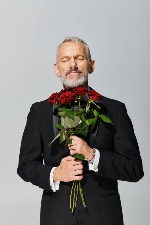 joyful handsome mature man in tuxedo holding red roses bouquet and smiling with closed eyes, banner