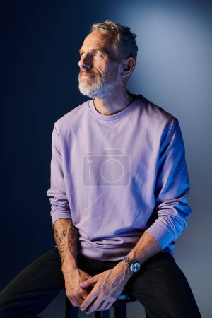 schöner bärtiger älterer Mann in lässigem lila Sweatshirt mit Accessoires, der lächelt und wegschaut