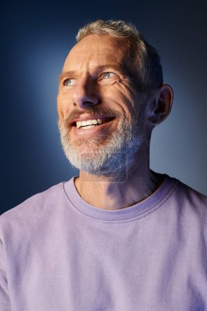 fröhlicher bärtiger älterer Mann in lässigem lila Sweatshirt mit Accessoires, der lächelt und wegschaut