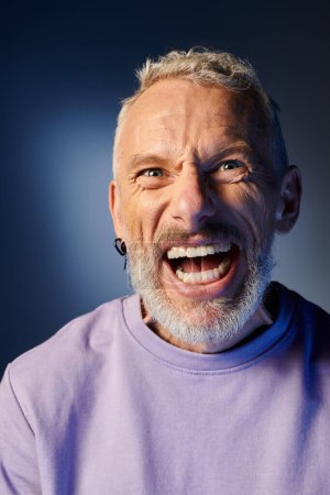 cheerful mature man with gray beard and casual trendy attire grimacing and looking at camera