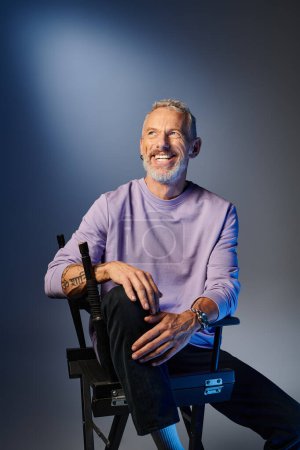 attractive joyful mature man in stylish purple sweatshirt sitting on chair and looking away