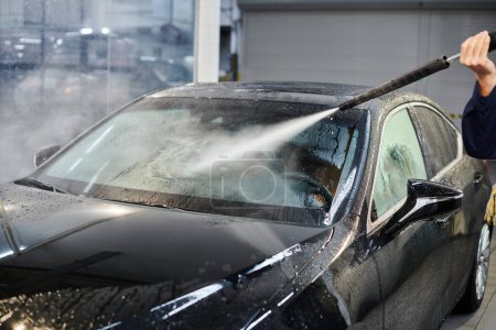 cropped view of devoted professional serviceman in uniform washing black car while in garage