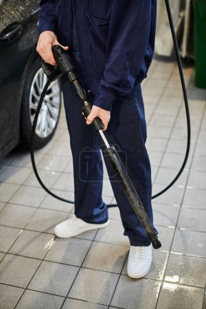 cropped view of hard working serviceman in blue uniform preparing to use hose to wash black car