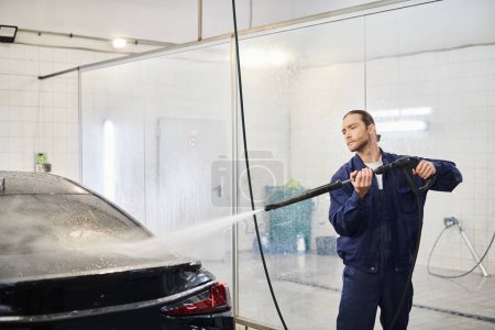 appealing devoted serviceman in comfy uniform with collected hair washing modern car in garage