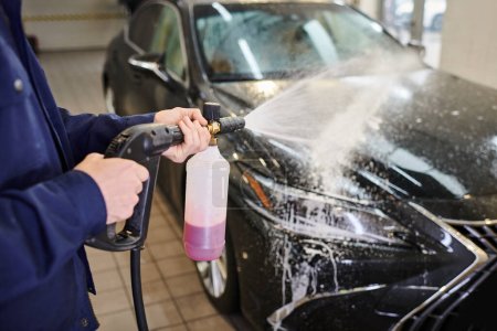 przycięty widok dedykowanego specjalisty ciężkiej pracy w niebieskim mundurze za pomocą mydła do mycia czarnego samochodu