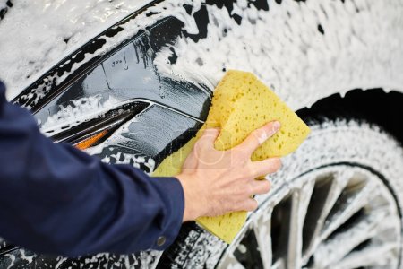 cropped view of hard working professional in uniform washing car using sponge and soap in garage