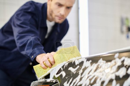 focus on soapy sponge in hands of blurred good looking serviceman in uniform washing black car