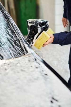 przycięty widok oddanego ciężko pracującego specjalisty w wygodnym, jednolitym samochodzie myjącym z gąbką mydlaną