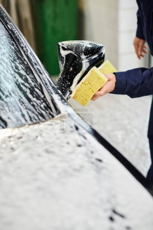cropped view of devoted hard working specialist in comfy uniform washing car with soapy sponge