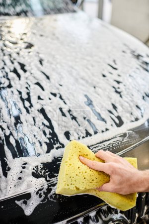 przycięty widok oddanego ciężko pracującego żołnierza w mundurze mycie czarny nowoczesny samochód z gąbką