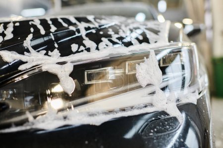 Objektfoto des Scheinwerfers eines schwarzen modernen Autos, das während des Waschdienstes in der Garage mit Seife bedeckt war