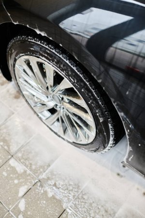 Objektfoto von glänzenden Reifen eines schwarzen modernen Autos, das während des Waschvorgangs in der Garage mit Seife bedeckt ist
