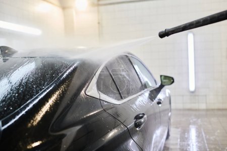 przycięty widok entuzjastycznego oddanego żołnierza myjącego czarny nowoczesny samochód z uwagą w garażu