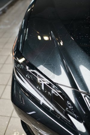 Objektfoto eines schwarzen modernen Autos mit seinen Scheinwerfern, die während des Waschvorgangs in der Garage geparkt waren