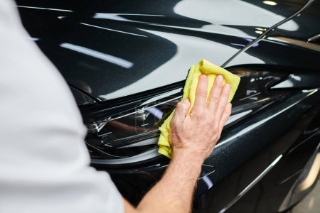 cropped view of hard working professional serviceman cleaning car with rag while in garage