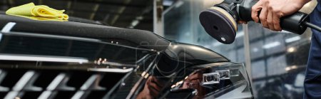 Téléchargez les photos : Vue recadrée de dur labeur professionnel dédié polissage voiture noire avec machine spéciale - en image libre de droit