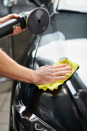 cropped view of devoted professional serviceman cleaning car with rag and holding polishing machine