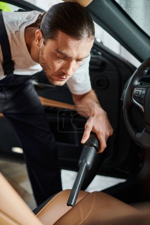 good looking professional serviceman in uniform with collected hair using vacuum cleaner in  car