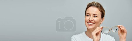 Photo for Beautiful cheerful woman with blonde hair and glasses looking away on gray backdrop, banner - Royalty Free Image