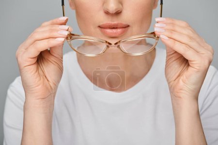 Ausgeschnittene Ansicht einer Frau in lässiger urbaner Kleidung mit Brille vor grauem Hintergrund