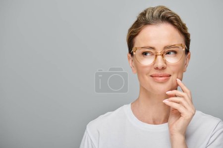 Photo for Good looking jolly woman with blonde hair and glasses in casual attire looking away on gray backdrop - Royalty Free Image