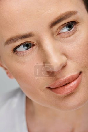 attraktives weibliches Model mit blonden Haaren und Kontaktlinsen posiert vor grauem Hintergrund und schaut weg