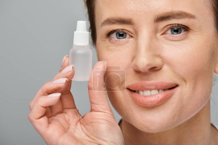 Photo for Cheerful good looking woman holding eye drops and looking straight at camera on gray backdrop - Royalty Free Image