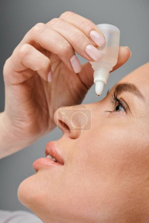 close up of attractive female model with blonde hair putting in eye drops while on gray backdrop