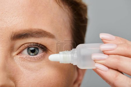 close up of appealing female model with blonde hair putting in eye drops on gray backdrop