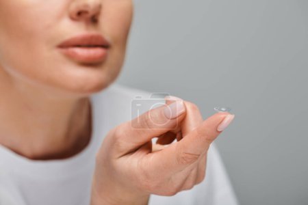 Ausgeschnittene Ansicht eines konzentrierten weiblichen Modells, das Kontaktlinsen sorgfältig auf grauem Hintergrund trägt