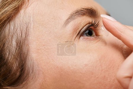 Nahaufnahme eines attraktiven weiblichen Modells, das seine Kontaktlinse trägt, während es auf grauem Hintergrund posiert