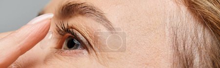 primer plano de la mujer guapa usando cuidadosamente su lente de contacto mientras posa sobre fondo gris