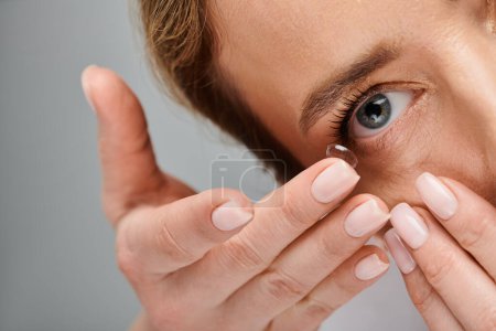 primer plano de la mujer guapa usando cuidadosamente su lente de contacto mientras posa sobre fondo gris