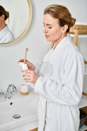 attractive blonde woman with collected hair in bathrobe brushing her teeth in front of mirror