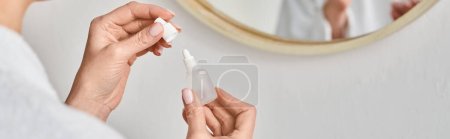 cropped view of adult woman in bathrobe using her eye drops in front of mirror in bathroom