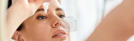 Photo for Attractive blonde woman with collected hair in bathrobe putting in eye drops in her bathroom, banner - Royalty Free Image