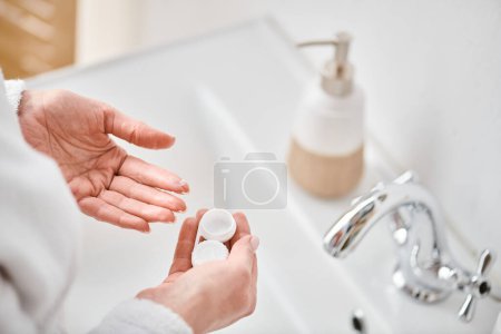 cropped view of adult woman in bathrobe holding her contact lenses before wearing them in bathroom
