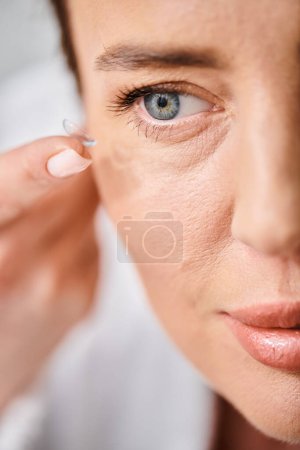 attraktive Frau im weißen bequemen Bademantel mit Kontaktlinsen in der Nähe von Spiegel im Badezimmer