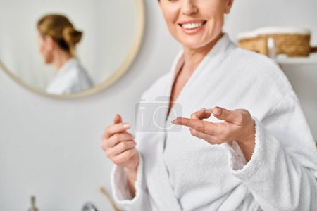 Photo for Good looking jolly woman in white comfy bathrobe wearing her contact lenses near mirror in bathroom - Royalty Free Image