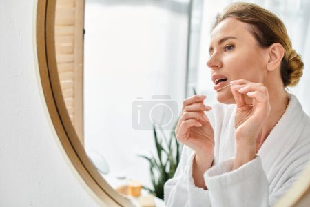 atractiva mujer rubia con pelo recogido en albornoz limpiando sus dientes con hilo dental