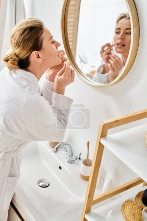 hermosa mujer rubia con pelo recogido en albornoz limpiando sus dientes con hilo dental