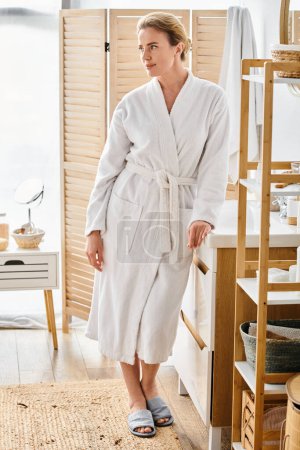 Photo for Appealing cheerful woman with blonde hair in white bathrobe posing in her bathroom and looking away - Royalty Free Image